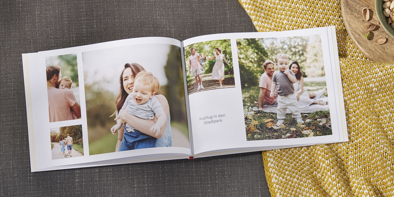 Na pohovke leží otvorená CEWE FOTOKNIHA v štýle „Our Family“. Na dvojstrane je niekoľko motívov rodiny v záhrade. Vpravo od fotoknihy je miska s pistáciami.